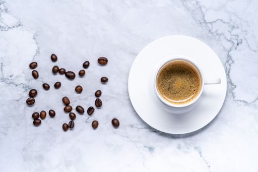A top view of a  cup of espresso and coffee beans on a marble table