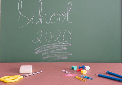 SCHOOL 2020 written on the green chalkboard behind the desk with colorful pins