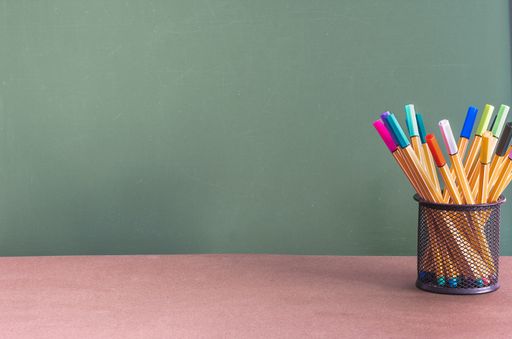 A green chalkboard with space for text behind the desk with colorful pens