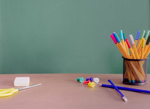 A green chalkboard with space for text behind the desk with colorful pens and pins