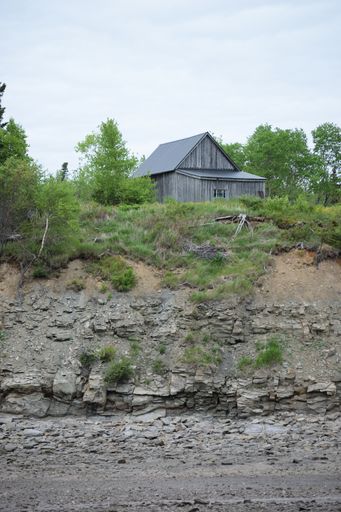 A vertical shot of a small wooden house near a rocky coast in Cumberland County, Canada