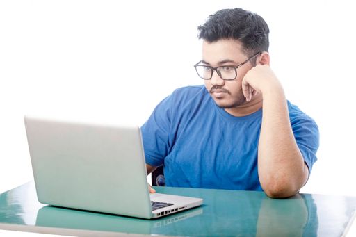Studio shot of a handsome young boy sitting and using a laptop and looking stressed isolated by white background