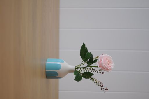 A vertical shot of a pink rose in a creative blue-white vase