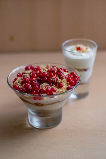 A vertical shot of a glass bowl of vanilla yogurt with currants on top on a beige background