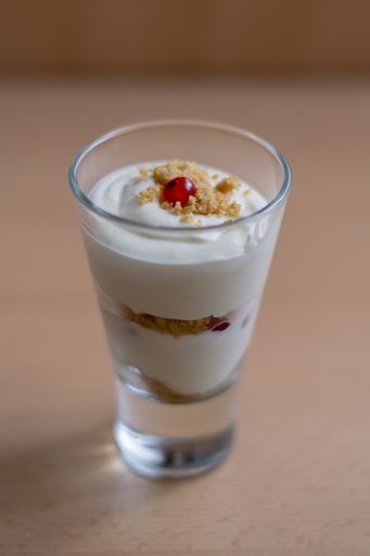 A vertical shot of a glass bowl of vanilla yogurt with currants on top on a beige background