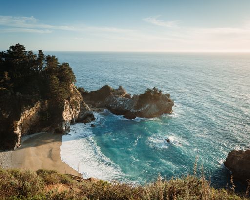 An aerial tranquil scenery of the ocean waves hitting the rocky beach during sunset