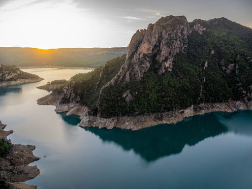A high angle shot of the tree-covered hill by the calm  and tranquil lake captured at sunset