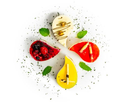 An overhead shot of four different teardrop-shaped cheesecakes on a white plate