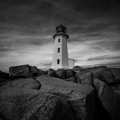 A low angle closeup of a white lighthouse surrounded by big textured rocks in greyscale