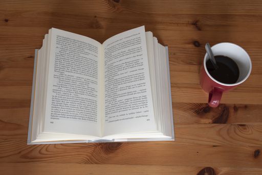 A high angle shot of a book and a cup of coffee on a wooden table