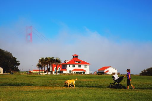 A female with a baby stroller and Old Coast Guard Station with Golden Gate Bridge in the background