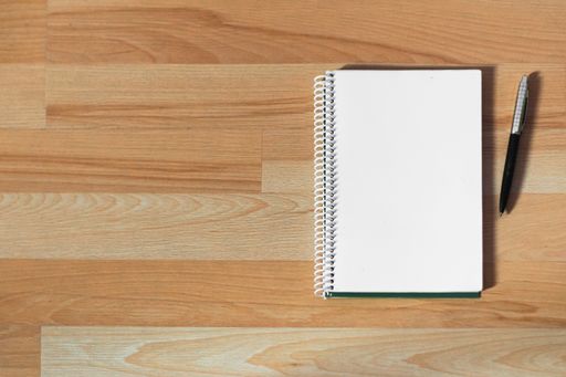 A high angle shot of a notebook with a pen on a wooden surface