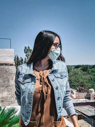 A vertical shot of a young Mexican female wearing  a surgical mask, glasses and a denim jacket