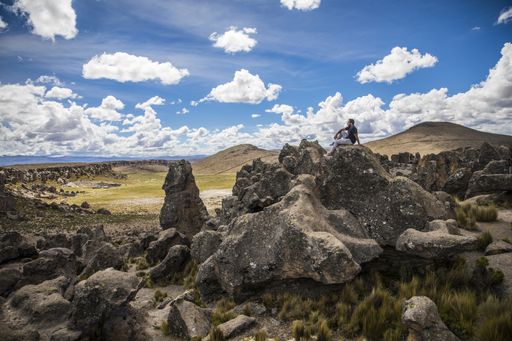 A beautiful view of a man sitting on huge rock formations with a cloudy blue sky in the background