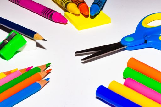 A vertical shot of colored pencils, scissor, eraser, and a notepad on a white table