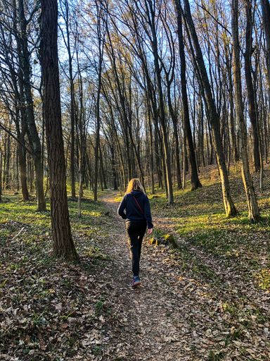 A vertical back view of a female in a jacket walking on a forest trail