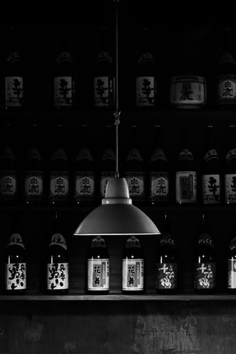 A vertical dramatic shot of a hanging black lamp on a background of bottles with Asian symbols