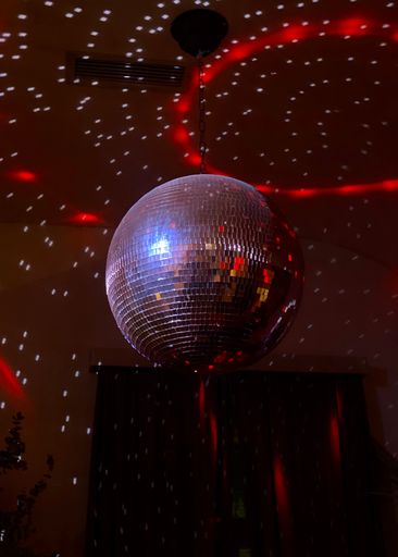A vertical closeup of the bright disco ball against the dark red background.