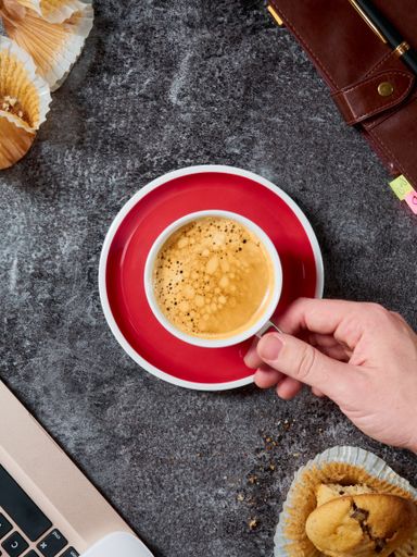 A vertical shot of a hand holding a cup of espresso in a saucer