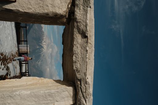A vertical of a stone monument against a Caucasian female looking at Dolomites in South Tyrol, Italy