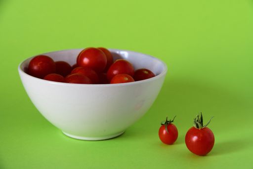 A close shot of small tomatoes in a white bowl on a green surface