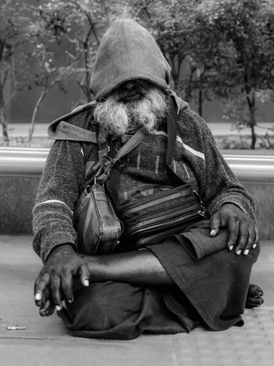 A vertical grayscale shot of a homeless Tamil Indian male sitting on the sidewalk in Kuala Lumpur, Malaysia