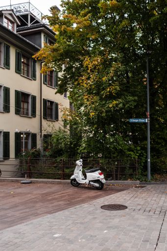 A Vertical shot of a white Vespa scooter in the street with trees in Saint Gallen in Switzerland