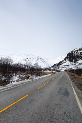 A vertical shot of a road against the background of snowy mountains. Hemsedal, Norway, Riksvei 52.