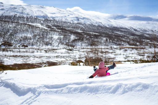 The little girl is sliding on the snow against the background of mountains. Hemsedal, Norway.