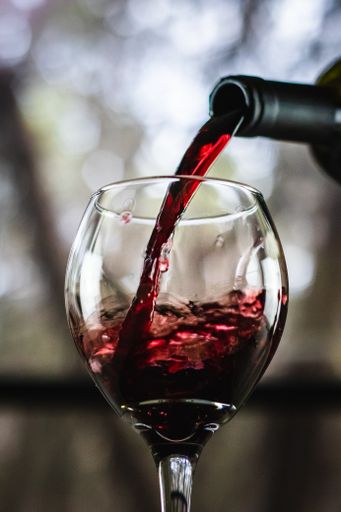 Red wine being poured from a bottle into a wine glass with a stem in front of an open window