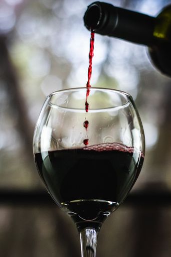 Red wine being poured from a bottle into a wine glass with a stem in front of an open window