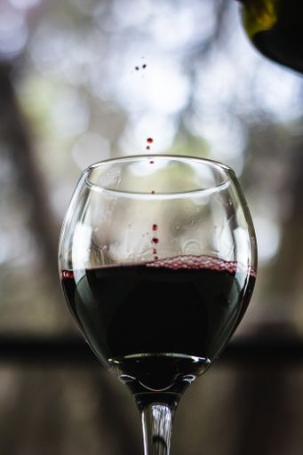 Red wine being poured from a bottle into a wine glass with a stem in front of an open window