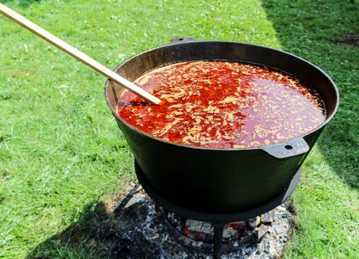 A close-up shot of a goulash soup in a big cast iron pot cooking on a bonfire outdoors