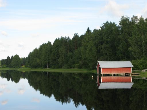 The reflection of a wooden cottage and the trees on a calm and tranquil lake captured in Finland