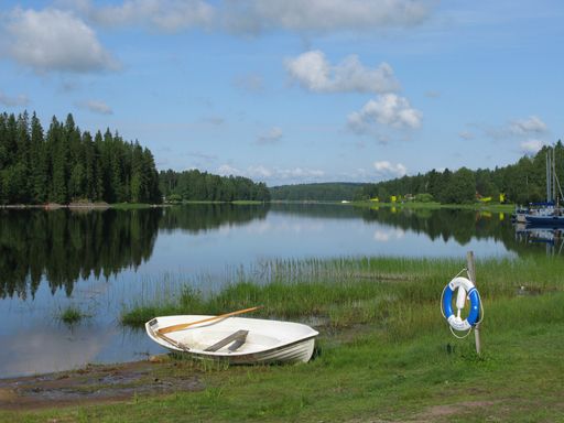 An abandoned rowboat on the side of a beautiful river reflecting the trees and the sky in Finland