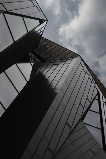 A low angle shot of a modern black glass building with cloudy sky in the background