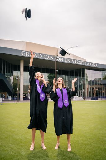 Two females happily throwing their caps in celebration of graduating from the Grand Canyon University