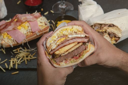 A big sandwich with various kinds of meat and corn and some burgers around