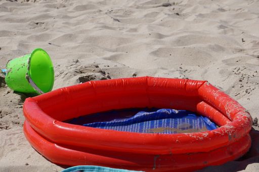 A closeup shot of a children's inflatable pool with no water and a toy bucket on the sand