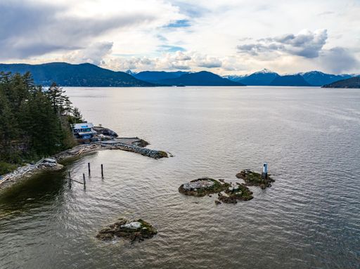 An areal shot of islands in the ocean and green trees on the beach of Horseshoe Bay against a cloudy blue sky and mountains in West Vancouver, Canada
