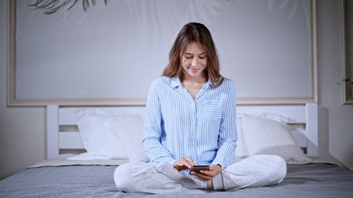 Caucasian young woman wearing pajamas and checking her phone while sitting on bed