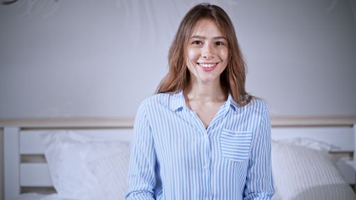 Caucasian young woman looking at the camera with a smile, wearing pajamas and sitting on bed