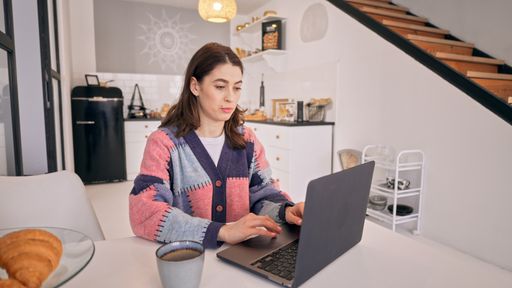 Caucasian young woman working on her laptop and drinking coffee in her house