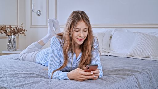 Caucasian young woman wearing pajamas and checking her phone while lying on bed