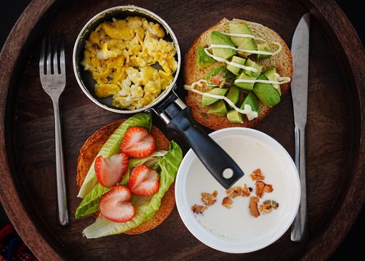 Top view of scrambled eggs in a pan, strawberries and lettuce on a toast and avocado on a toast