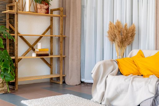 Cozy and comfortable living area: wall decorated with fabrics, sofa with yellow cushions and wooden shelf with decorative street lamps with candle.