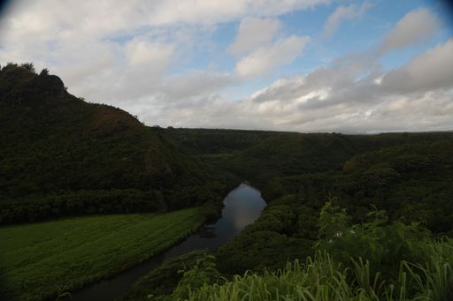 A beautiful wide shot of a narrow river flowing between green grass hills under a cloudy sky