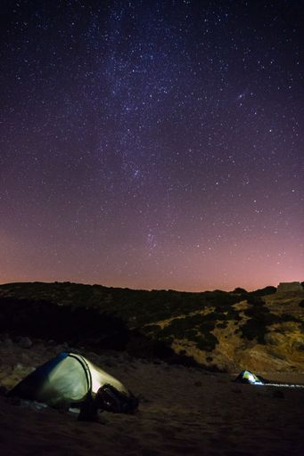 The two tents next to a huge rocky cliff on a beach at night with stars Figueira, Portugal