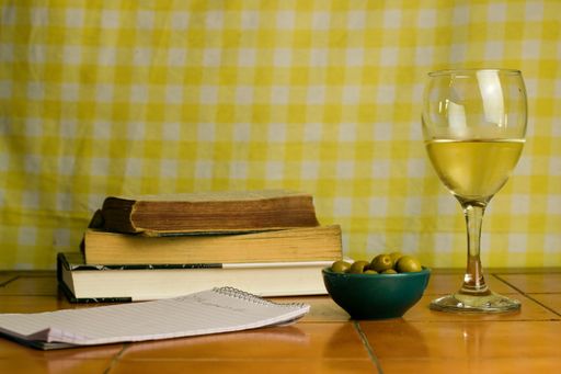 A glass of white wine and green olives, books  on wooden table