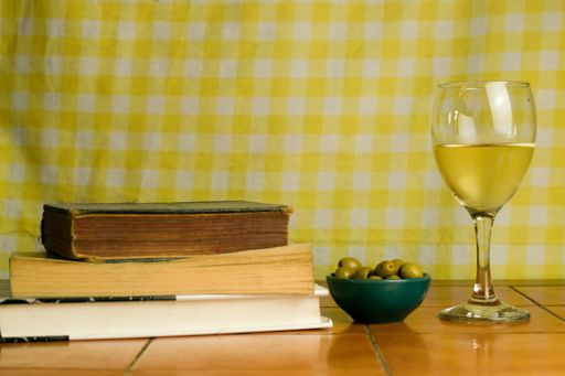 A glass of white wine and green olives, books  on wooden table